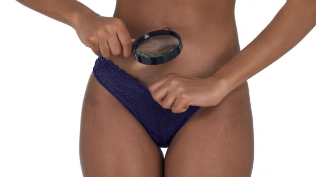Close-up of a woman looking under her panties through the magnifying glass and showing thumb up. Isolated, on white background