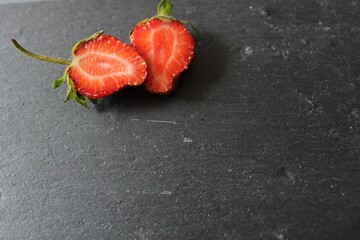 on a black background grey stone there are two halves of strawberries cut on the left side food background with a place to insert text