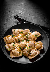 Meat dumplings - russian pelmeni, ravioli with meat in black plate on Dark grey black slate background