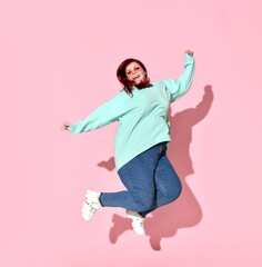 Active young female with overweight in casual attire and glasses jumping up full of happiness and...