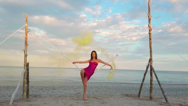 Ragazza con fumogeno giallo e vestito fucsia si dondola nell'altalena in riva al mare