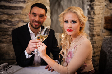 Romance and dating concept. Young couple man and woman with champagne glasses celebrating and toasting in restaurant. Two people male and female in elegant evening suit and dress on romantic dinner