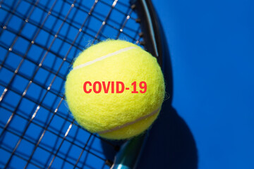 Close-up tennis ball on racket and blue background. Added red text COVID-19.