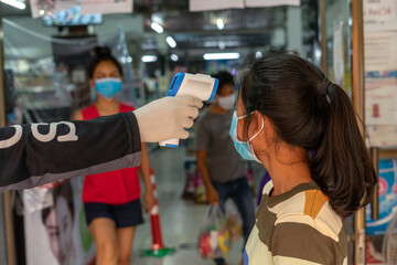 closeup of infrared forehead thermometer (gun) to check body temperature with blurred asian girl on background for Coronavirus, virus symptoms epidemic virus outbreak concept ,Covid-19.