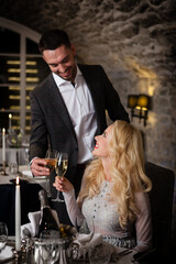 Romance and dating concept. Young couple man and woman with champagne glasses celebrating and toasting in restaurant. Two people male and female in elegant evening suit and dress on romantic dinner