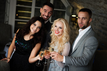 Party, holiday with friends concept. Four people with champagne glasses celebrating and toasting in restaurant. Two men and two women in elegant evening clothes, suits and dresses night out indoors