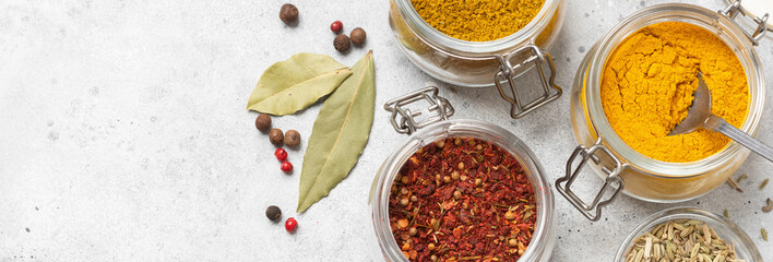 Spices and condiments in glass jars on a light gray table. Spices close-up with space for text. The view from the top. Banner