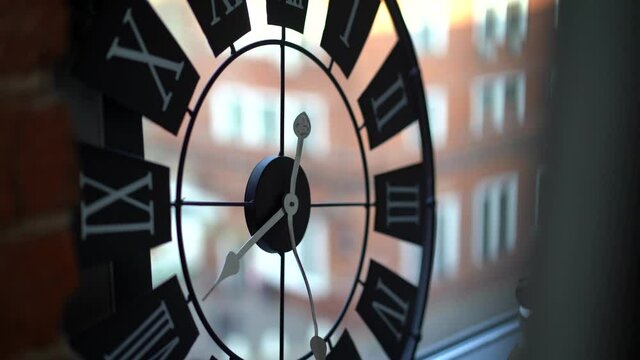 Subject: black wall clock with white Roman numerals and white hands on the background of the window, close-up