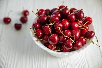ripe cherries in a white plate on a white wooden background. Vegetarian concept, food.
