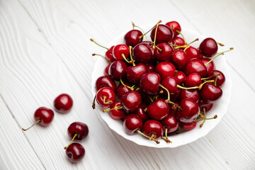 Fototapeta na wymiar ripe cherries in a white plate on a white wooden background. Vegetarian concept, food. 