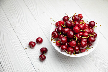 ripe cherries in a white plate on a white wooden background. Vegetarian concept, food.
