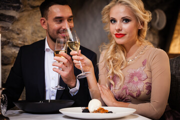 Romance and dating concept. Young couple man and woman with champagne glasses celebrating and toasting in restaurant. Two people male and female in elegant evening suit and dress on romantic dinner