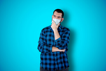 Caucasian handsome man isolated on blue background thinking an idea while looking up using mask. Coronavirus concept