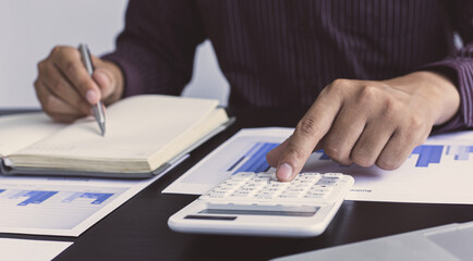 Young male business man holding a calculator to calculate financial graph data in the room.