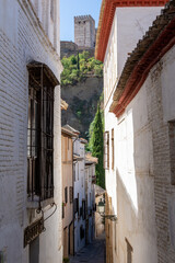 Narrow streets of the Granada neighborhood of Albaicín with the towers of the Alcazaba of the Alhambra in the background