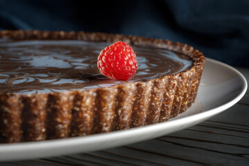 Chocolate cake with nuts, laid on a plate. On the cake lies a beautiful raspberry berry.