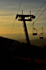 Ski chair lift in the mountains at orange sunrise. Vertical photo.