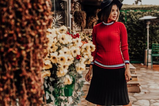 Beautiful model posing for photos on the street. Wearing black skirt, red blouse and hat.