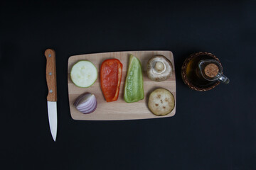 cut vegetables on cutting board, bottle of salad oil and a knife isolated on black background flat lay