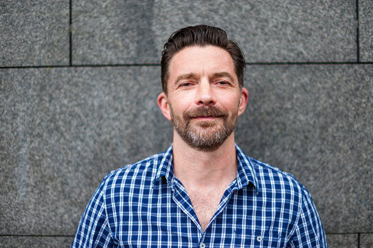 Portrait of confident handsome man standing against gray wall in city