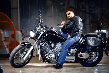 Fototapeta na wymiar Cool bearded man biker in sunglasses sitting on his motorbike and smoking cigar