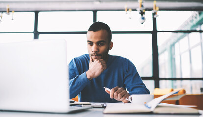 Young thoughtful afro american male international student watching training webinar about marketing...