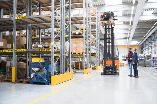 Two men and worker on forklift in high rack warehouse