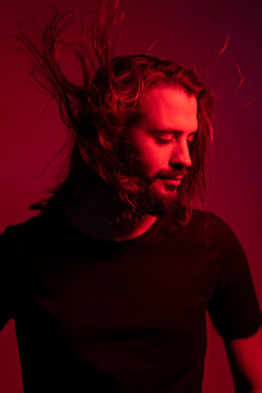 Portrait Of Red Illuminated Young Man With Blowing Hair Against Red Background