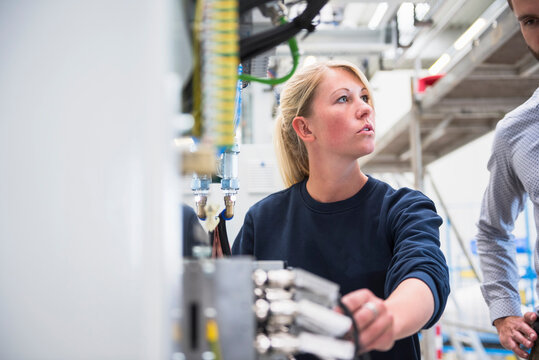 Young woman at a machine in a factory talking to man