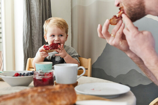 Portrait of little boy eating bread with jam watching his father