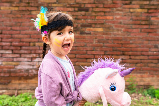 Portrait of girl with braids and feather headdress riding a pink unicorn