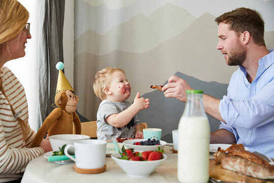 Smeared little boy with his parents at breakfast table