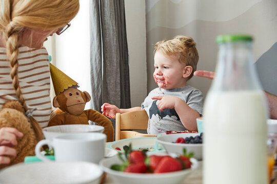 Smeared little boy at breakfast table looking at his soft toy