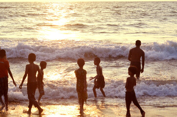 A group of enthusiastic young boys on the beach silhouette, waiting in anticipation of a sea wave. 
