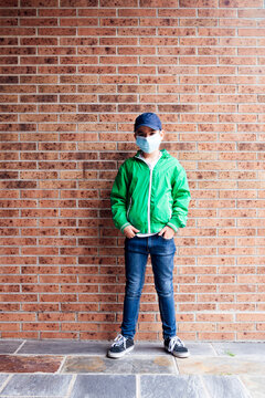 Boy wearing protective mask standing in front of a brick wall