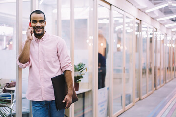 Portrait of cheerful young male employee of architect company happy to hear best friend on phone conversation during work break in coworking office with free wireless connection to fast 4G internet