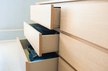 Open chest of drawers made of wood, side view. Inside are things, clothes, jeans. Close-up.