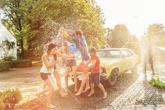 Friends washing yellow vintage car in summer having fun