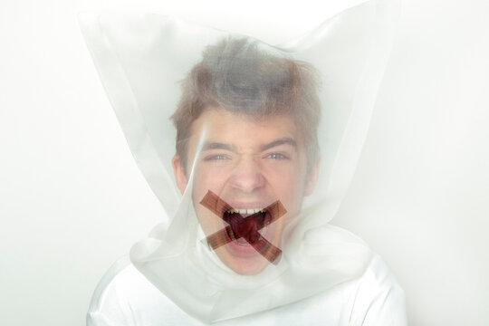 Portrait of screaming teenage boy wearing  transparent mask with cross on his mouth