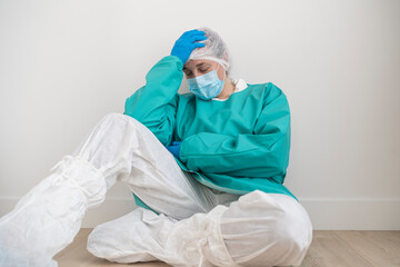 Exhausted woman wearing personal protective equipment sitting on the floor