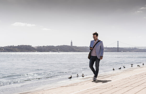 Young man walking on the waterfront using cell phone