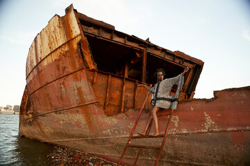 Woman wearing dress and sitting on rusty ship wreck