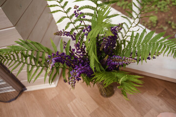 a bouquet of lupins and fern stands in a vase