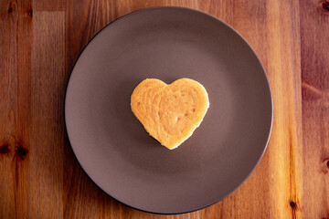 A heart-shaped pancake lies on a brown bench on a wooden table