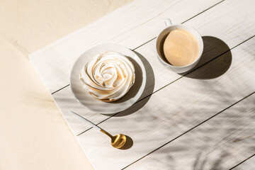 Lemon meringue little pie on a wooden board, table on a palm beach outdoor cafe in the shadows of palm branches. Continental breakfast with a cup of coffee.