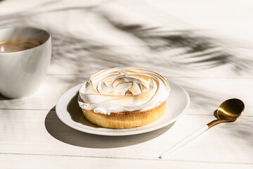 Lemon meringue little pie on a wooden board, table on a palm beach outdoor cafe in the shadows of palm branches. Continental breakfast with a cup of coffee.