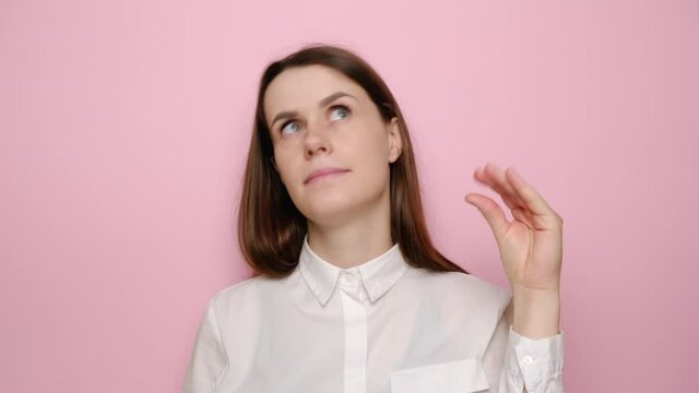 Portrait of boring young brunette woman posing showing blah blah gesture ja jaja hand, dressed in white shirt, isolated over pink studio background. People sincere emotions, lifestyle concept