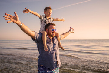 Happy father and son having quality family time on the beach on sunset on summer holidays. Lifestyle, vacation, happiness, joy concept - obrazy, fototapety, plakaty