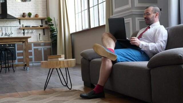 Work At Home In Quarantine. Businessman On The Couch Chatting In Video Chat. A Man In Shorts And A Tie.