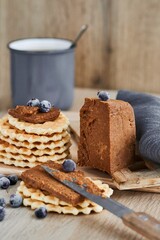 Viennese waffles with Norwegian brunost cheese and blueberries with a cup of coffee in the background. Breakfast with Traditional Scandinavian brown cheese